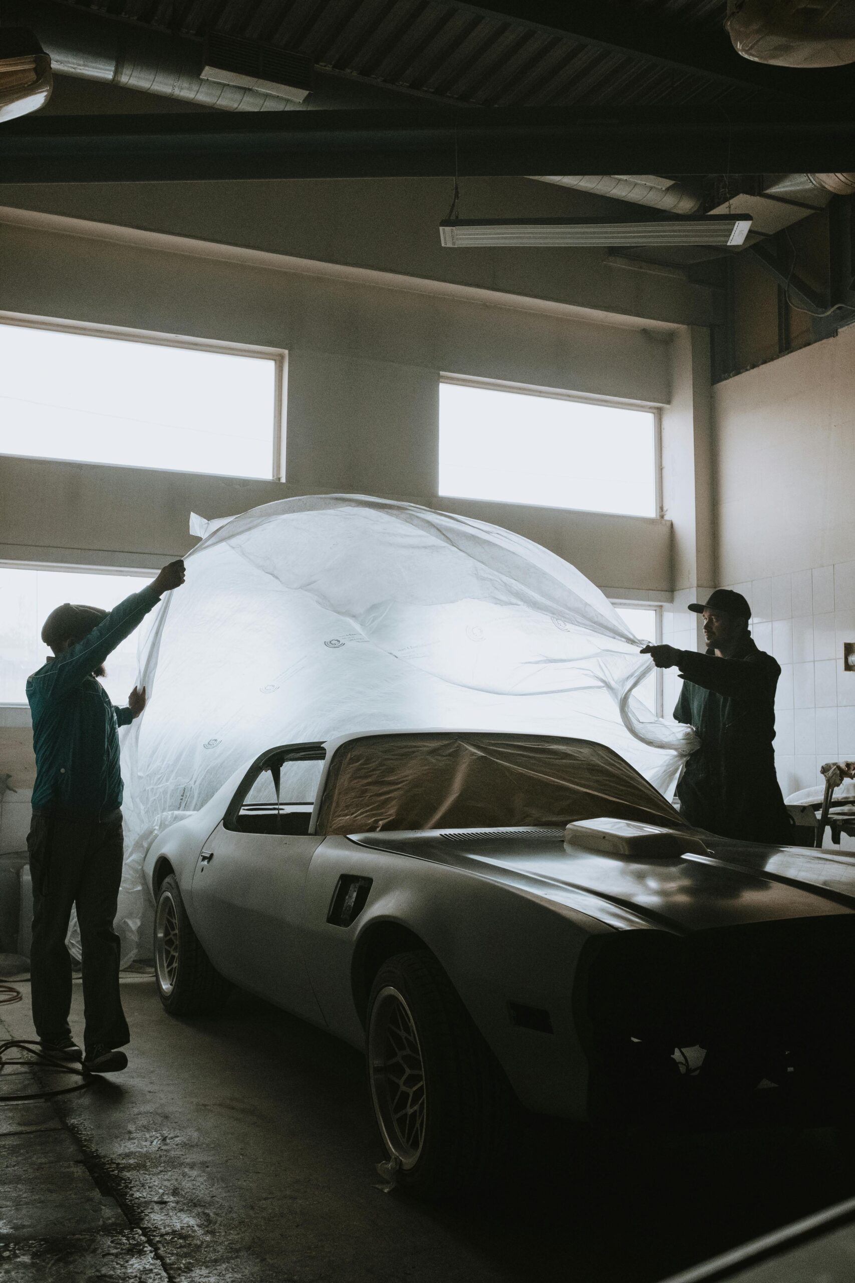 Mechanics working on classic car restoration inside a well-lit garage space.