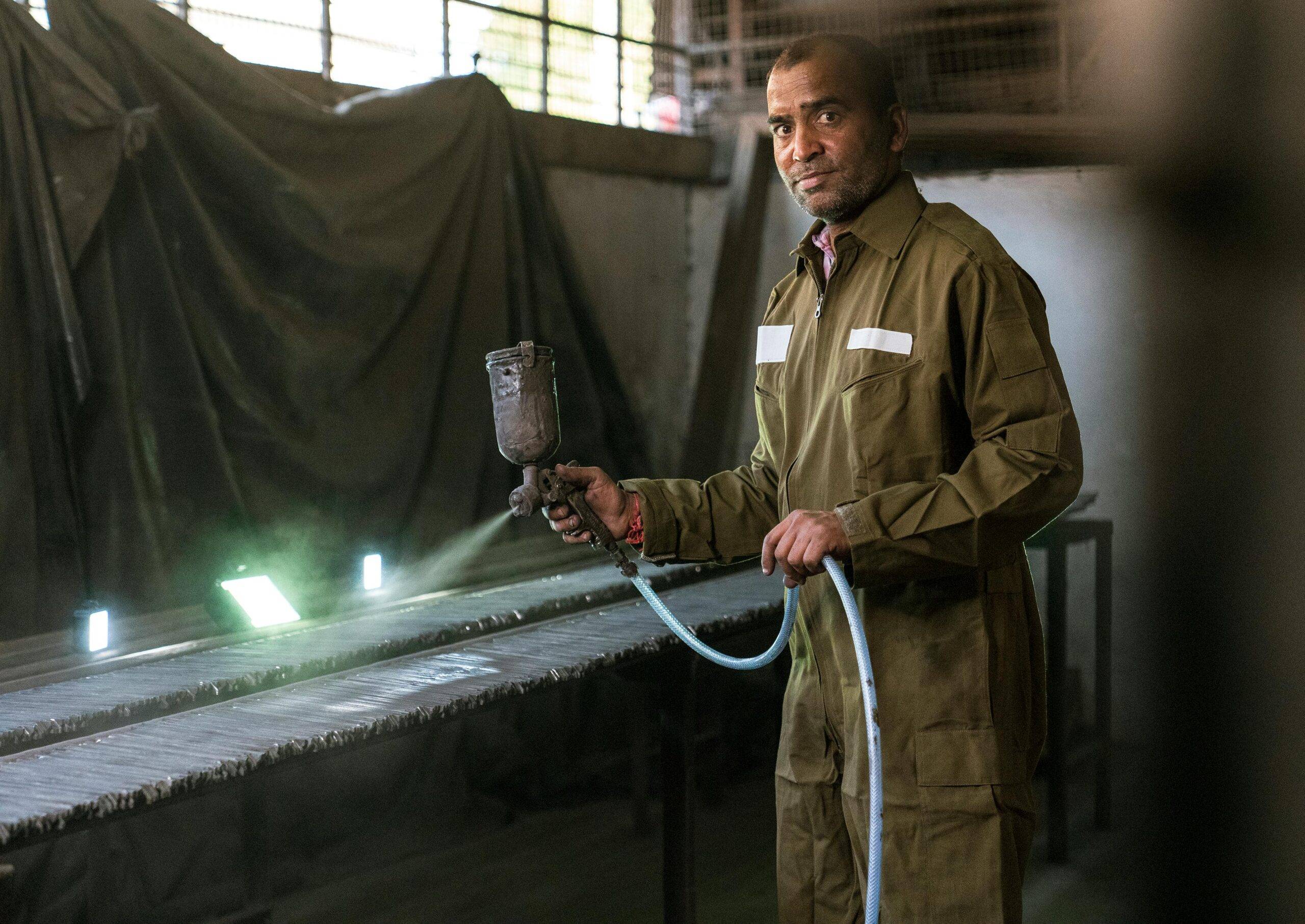 Worker in protective gear spraying in an industrial setting with focused expression.