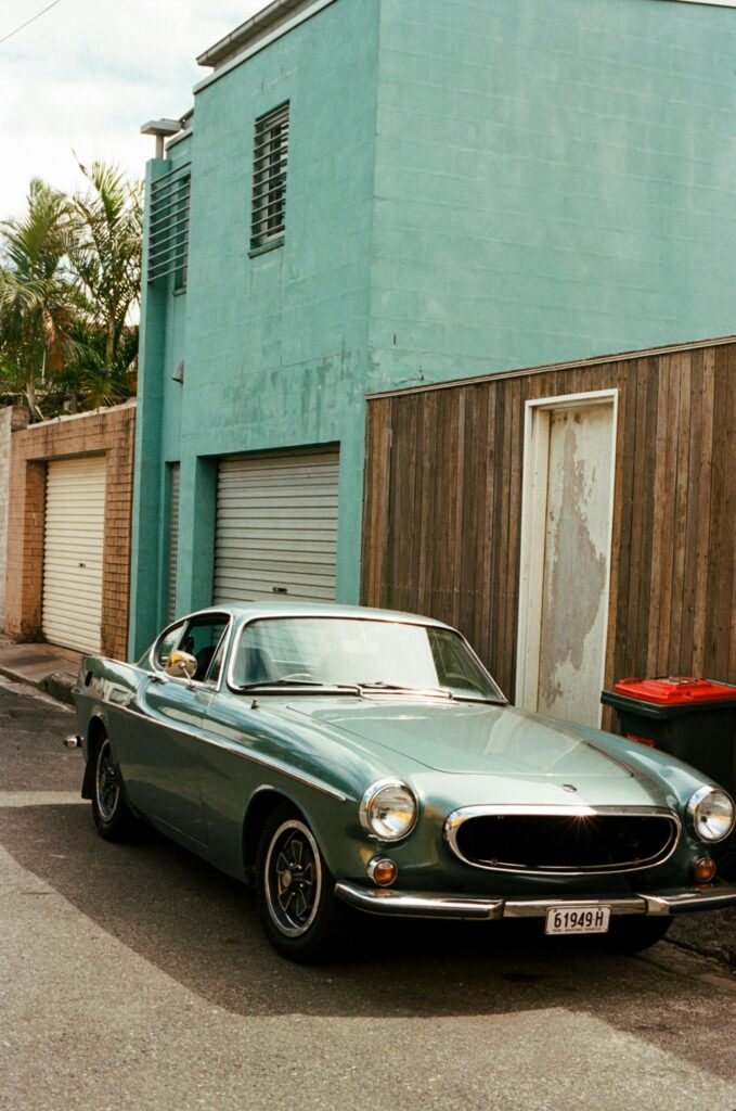 A classic green coupe parked beside a turquoise building on a sunny day.